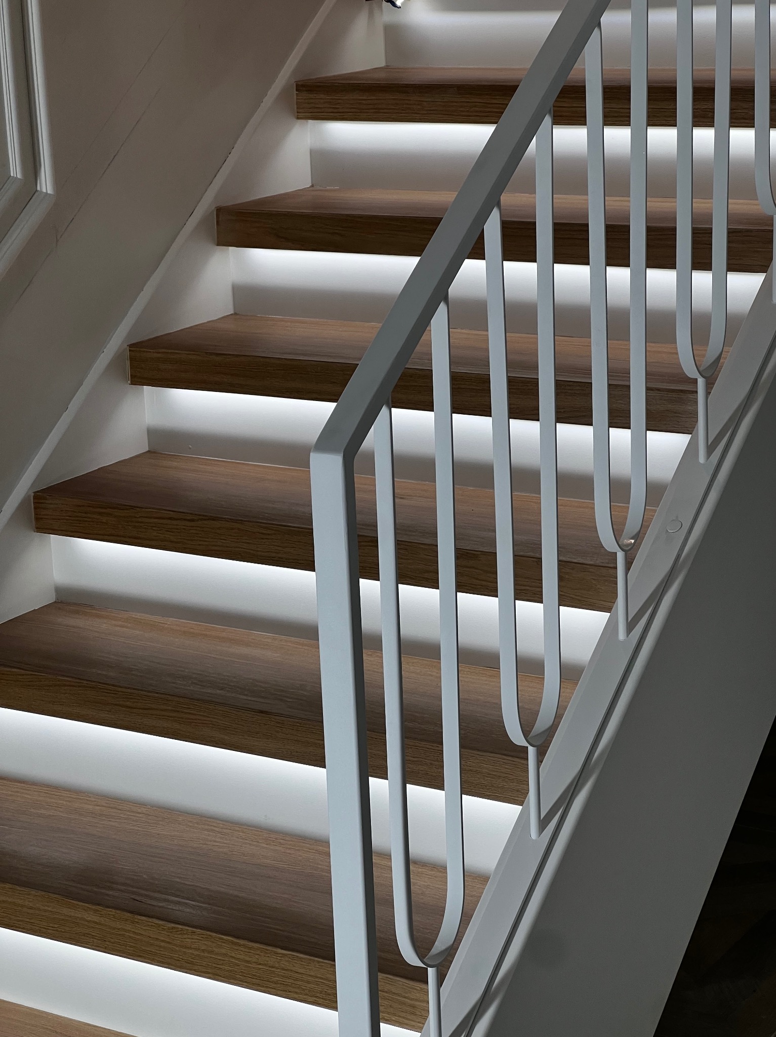 Nowoczesne schody drewniane z podświetleniem LED i białą, minimalistyczną balustradą. Ujęcie z dołu, podkreślające detale wykończenia i oświetlenie.