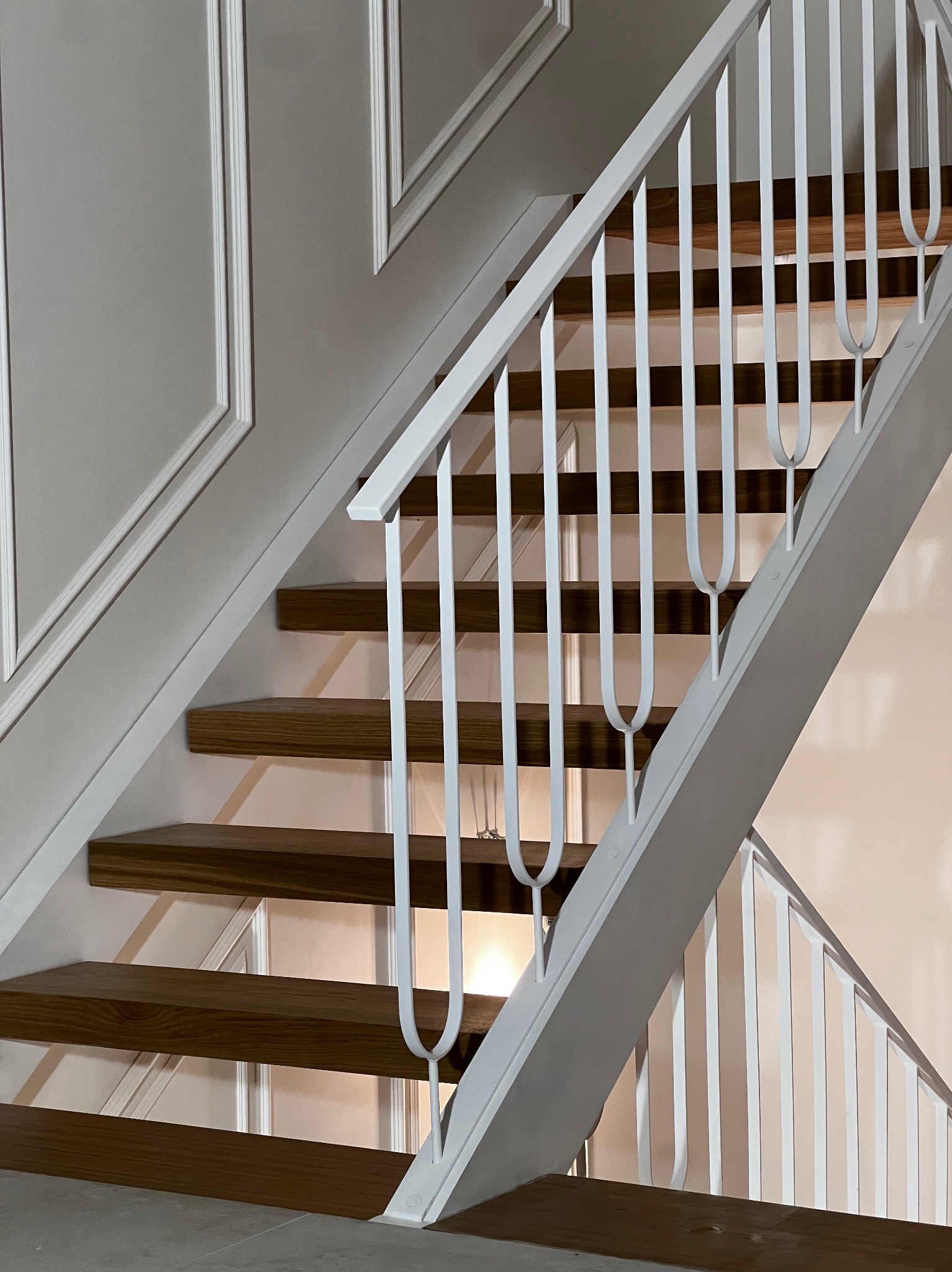 Nowoczesne schody z drewnianymi stopniami i białą, metalową balustradą o minimalistycznym designie. Ściana z dekoracyjnymi listwami. Ujęcie z dołu, podkreślające geometrię.