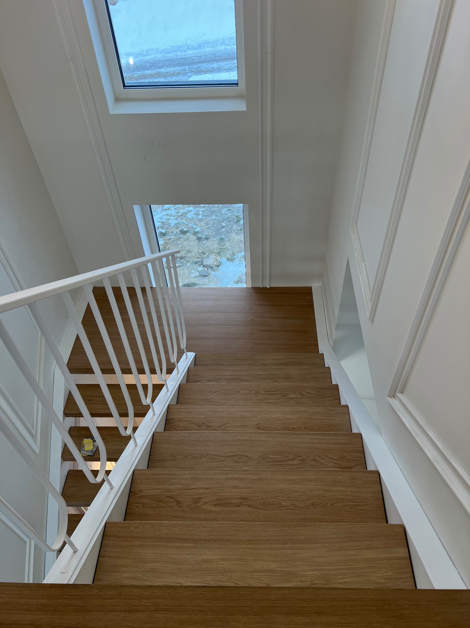 Nowoczesne schody drewniane z białymi poręczami, widok z góry. Naturalne oświetlenie z okna dachowego. Minimalistyczny design i jasna kolorystyka.