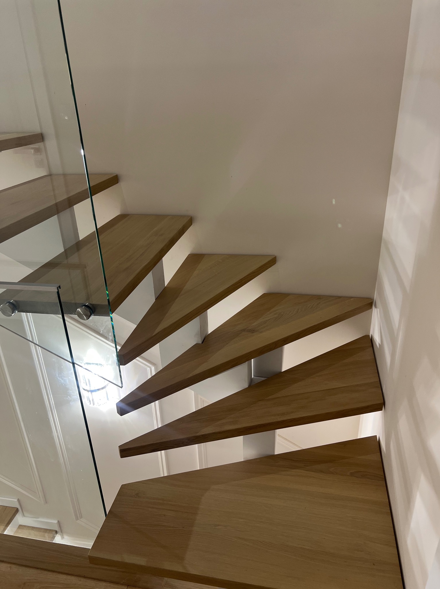 Nowoczesne schody z drewnianymi stopniami i szklaną balustradą, widok z dołu, podkreślający minimalistyczny design i jasne wykończenie wnętrza.