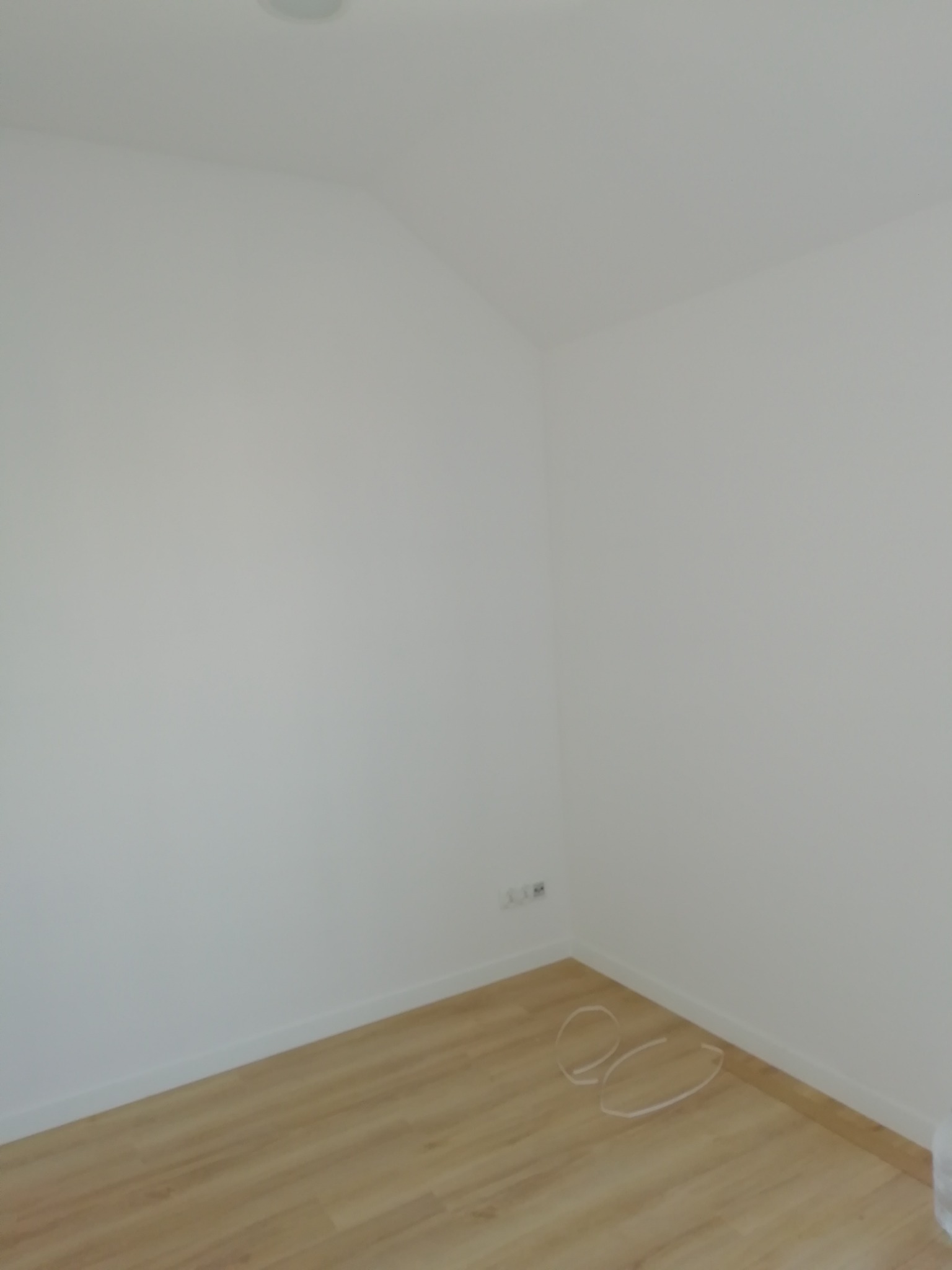 Pusty, świeżo pomalowany pokój z drewnianą podłogą i widocznymi kablami wystającymi ze ściany.