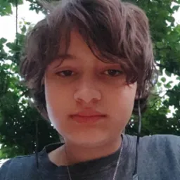 Portret młodego mężczyzny z Łasku, słuchającego muzyki na tle zieleni, z delikatnym uśmiechem.