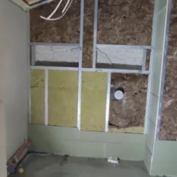 Poddasze w trakcie ocieplania: widoczne drewniane krokwie, folia paroizolacyjna, wełna mineralna między profilami metalowymi oraz fragment wylewki podłogowej.