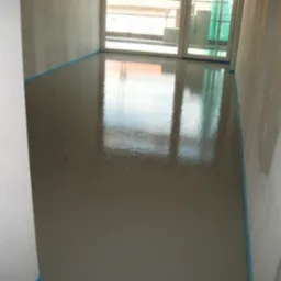 Świeżo wylana, samopoziomująca posadzka z widocznym odbiciem okna i zabezpieczającą, niebieską taśmą przy ścianach.