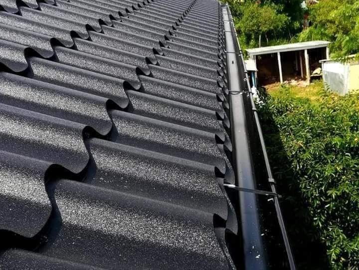 Czarny, metalowy dach z rynną w Warszawie, widok z góry na tle zieleni i małego budynku gospodarczego.