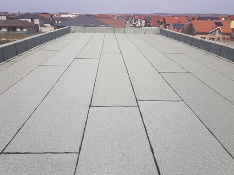 Nowe, płaskie pokrycie dachu z papy termozgrzewalnej, widok z góry, z obróbkami blacharskimi na krawędziach, w tle zabudowa jednorodzinna.