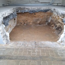 Rem-Ekspert Oleh Yefremov - Wyburzona podłoga z odsłoniętą ziemią, widoczne fragmenty gruzu i izolacji. Prace przygotowawcze do remontu, z bliska, z perspektywy chodnika.