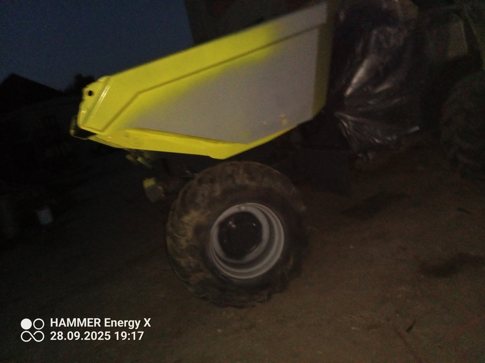 Żółto-szara, odnowiona przyczepka rolnicza z kołem, po renowacji. Widoczne ślady użytkowania na oponie. Niska jakość zdjęcia.