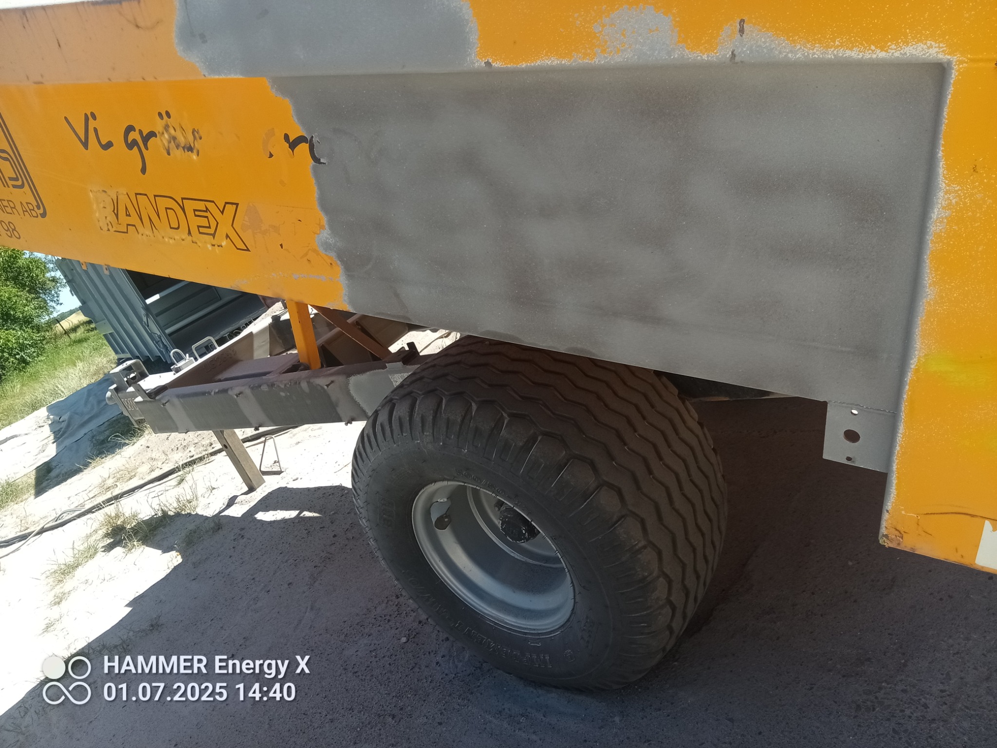 Żółta przyczepa z szarym fragmentem po piaskowaniu, widoczne koło. Częściowo usunięta farba odsłania metal. Napis 'RANDEX' na boku.