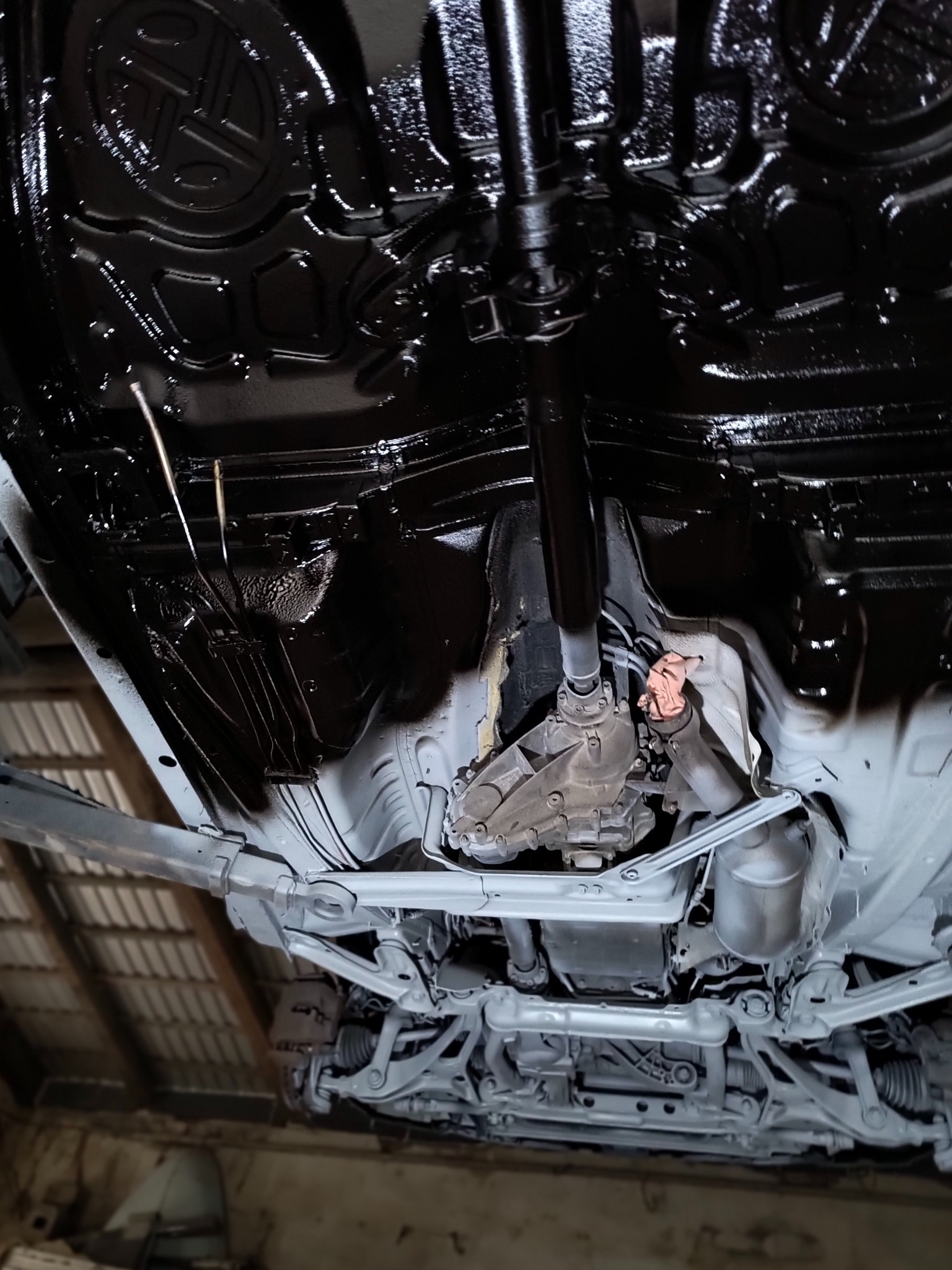 Podwozie auta po zabezpieczeniu antykorozyjnym. Część elementów pomalowana na czarno, część na szaro, widoczne detale zawieszenia i układu napędowego.