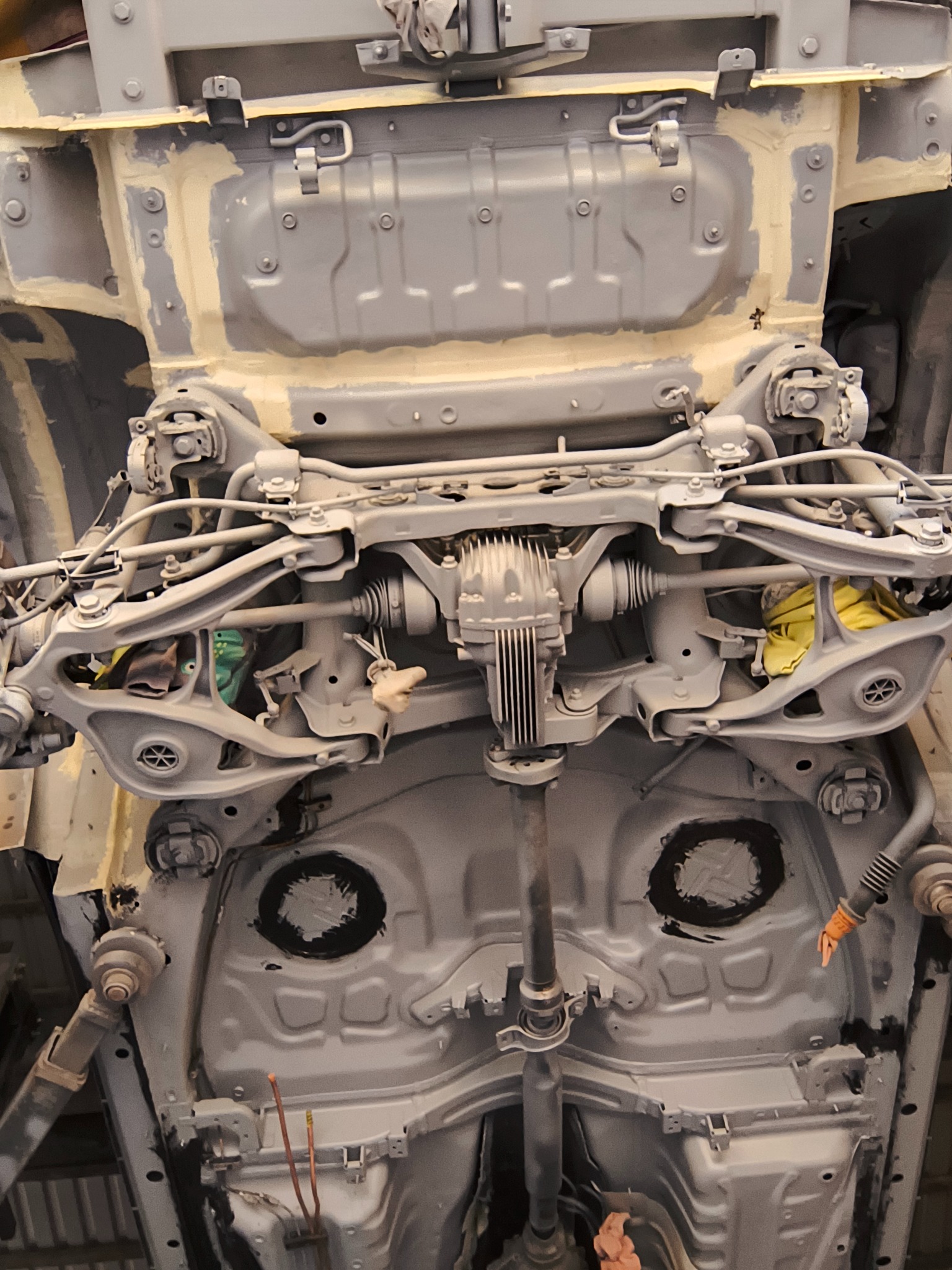 Podwozie samochodu po piaskowaniu i wstępnym malowaniu, widoczne elementy zawieszenia i karoserii w szarym podkładzie, przygotowane do dalszych prac lakierniczych.