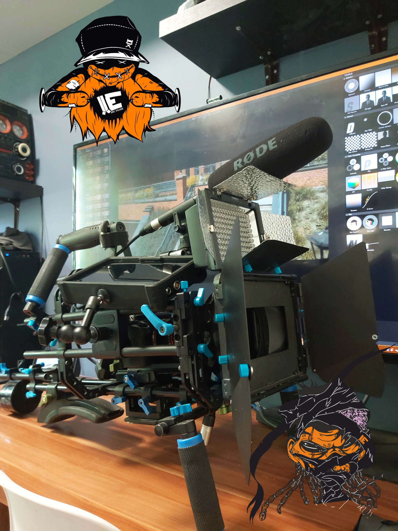 Profesjonalna kamera filmowa z mikrofonem RODE i osprzętem na drewnianym biurku, z widocznym monitorem z oprogramowaniem do edycji w tle. Na obraz nałożone grafiki w stylu graffiti.