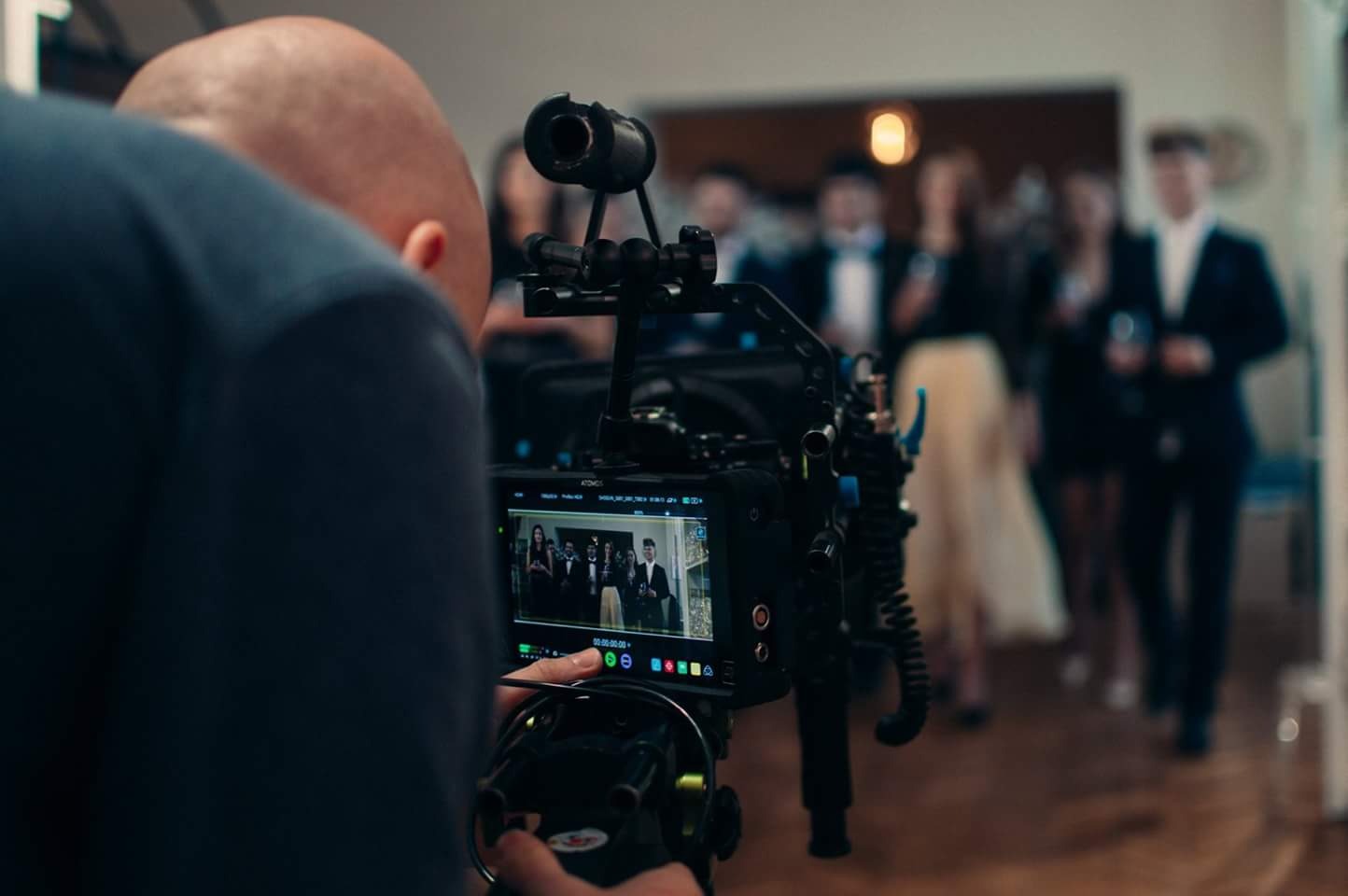 Operator kamery filmuje grupę elegancko ubranych osób podczas uroczystości, widok zza kamery z podglądem nagrywanego materiału.