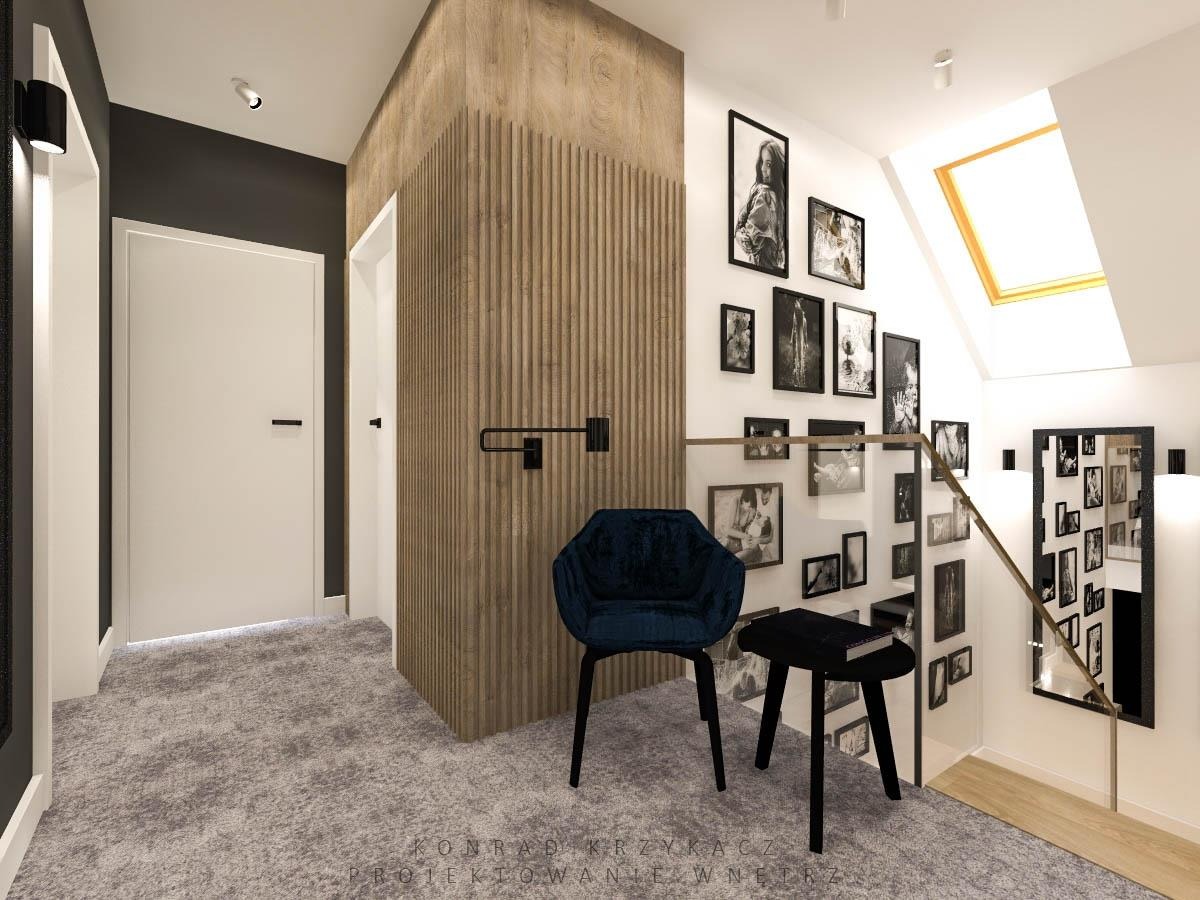 Hall z drewnianą ścianą z pionowych listew, galerią czarno-białych zdjęć, ciemnoniebieskim fotelem i czarnym stolikiem pomocniczym.