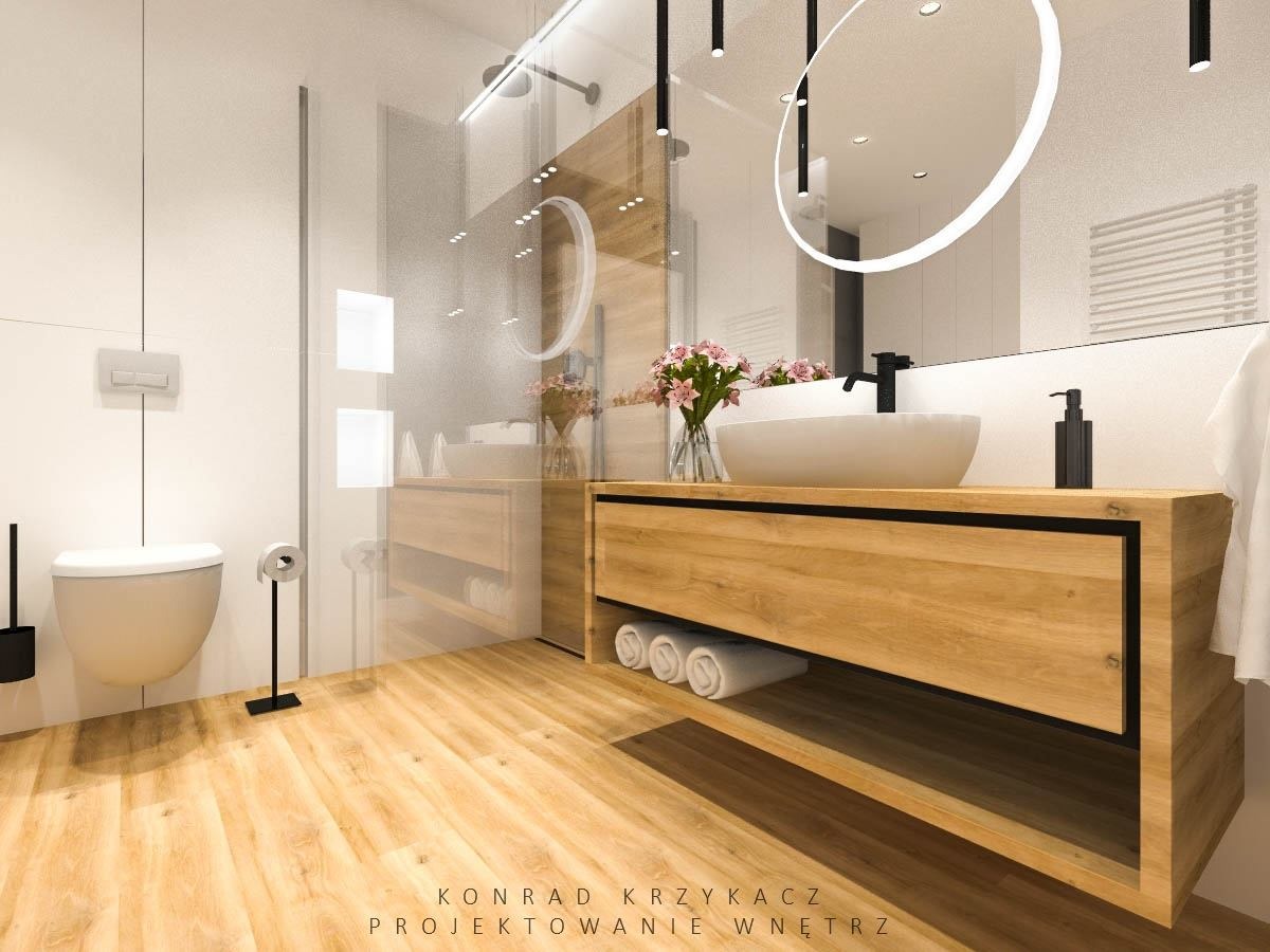 Nowoczesna łazienka z drewnianą szafką pod umywalką, okrągłym lustrem z podświetleniem LED, białymi ręcznikami i kwiatami w wazonie.