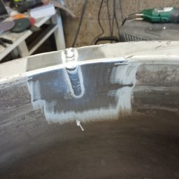 KUBA SZEWCZYK LOFTCRAFT - Fragment spawanej obręczy koła z widocznymi śladami szlifowania i spoiną, w tle warsztatowe narzędzia.