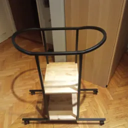 Metalowy wózek transportowy z drewnianymi półkami na kółkach, stojący na parkiecie ułożonym w jodełkę.