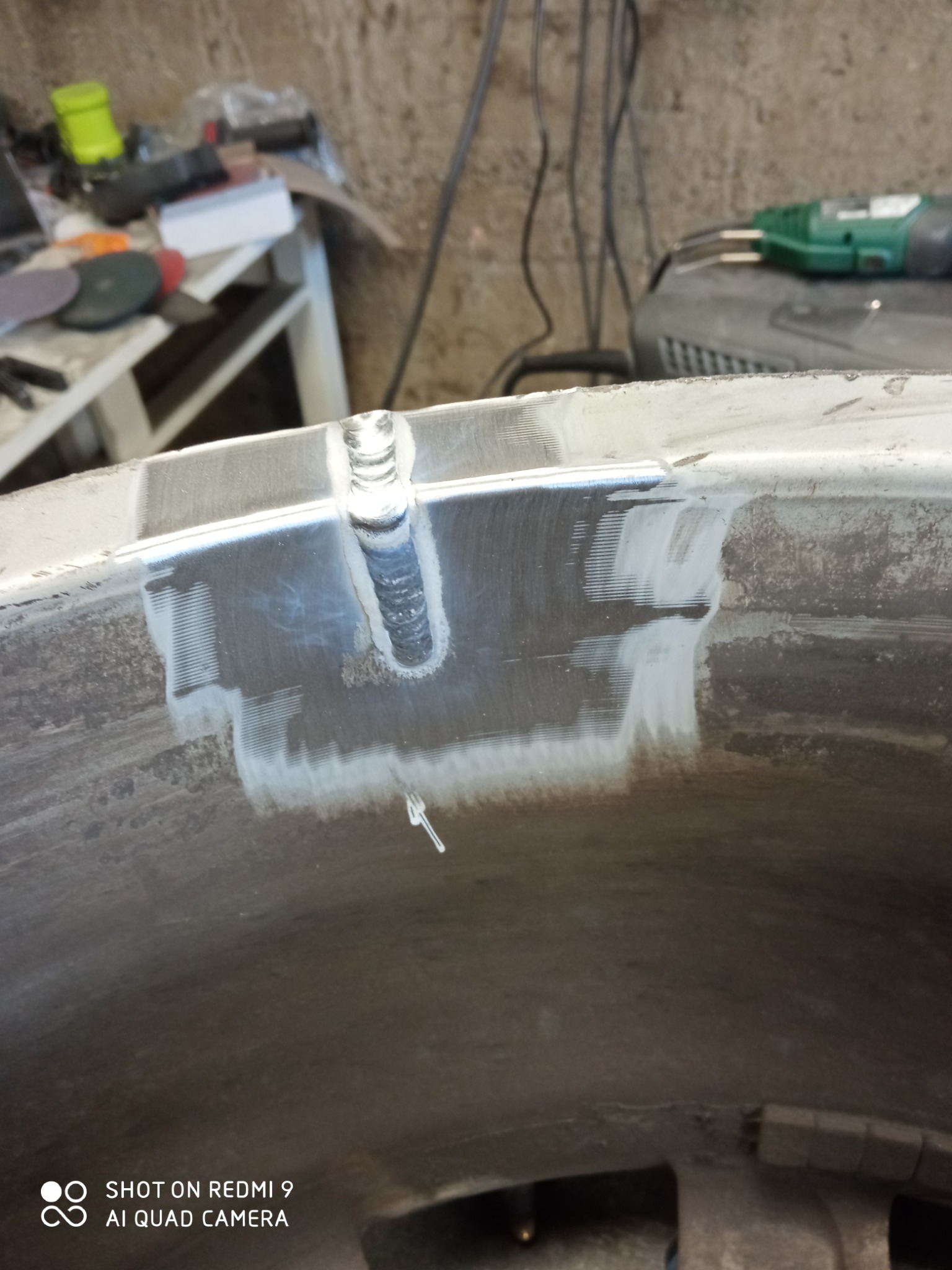 Fragment spawanej obręczy koła z widocznymi śladami szlifowania i spoiną, w tle warsztatowe narzędzia.