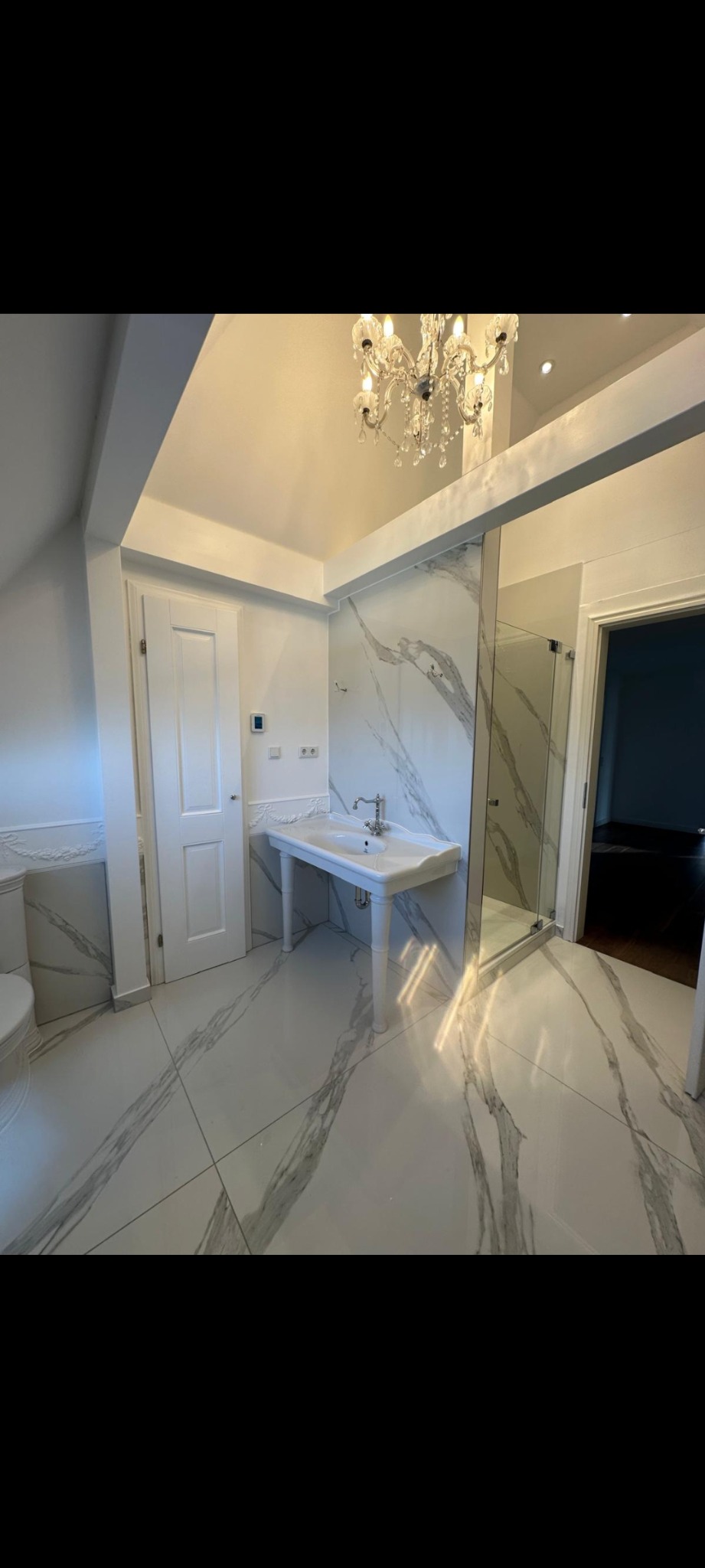 Elegancka łazienka w Tuczępy z marmurowymi płytkami, białą armaturą i kryształowym żyrandolem. Kabina prysznicowa ze szklanymi drzwiami. Nowoczesny design.