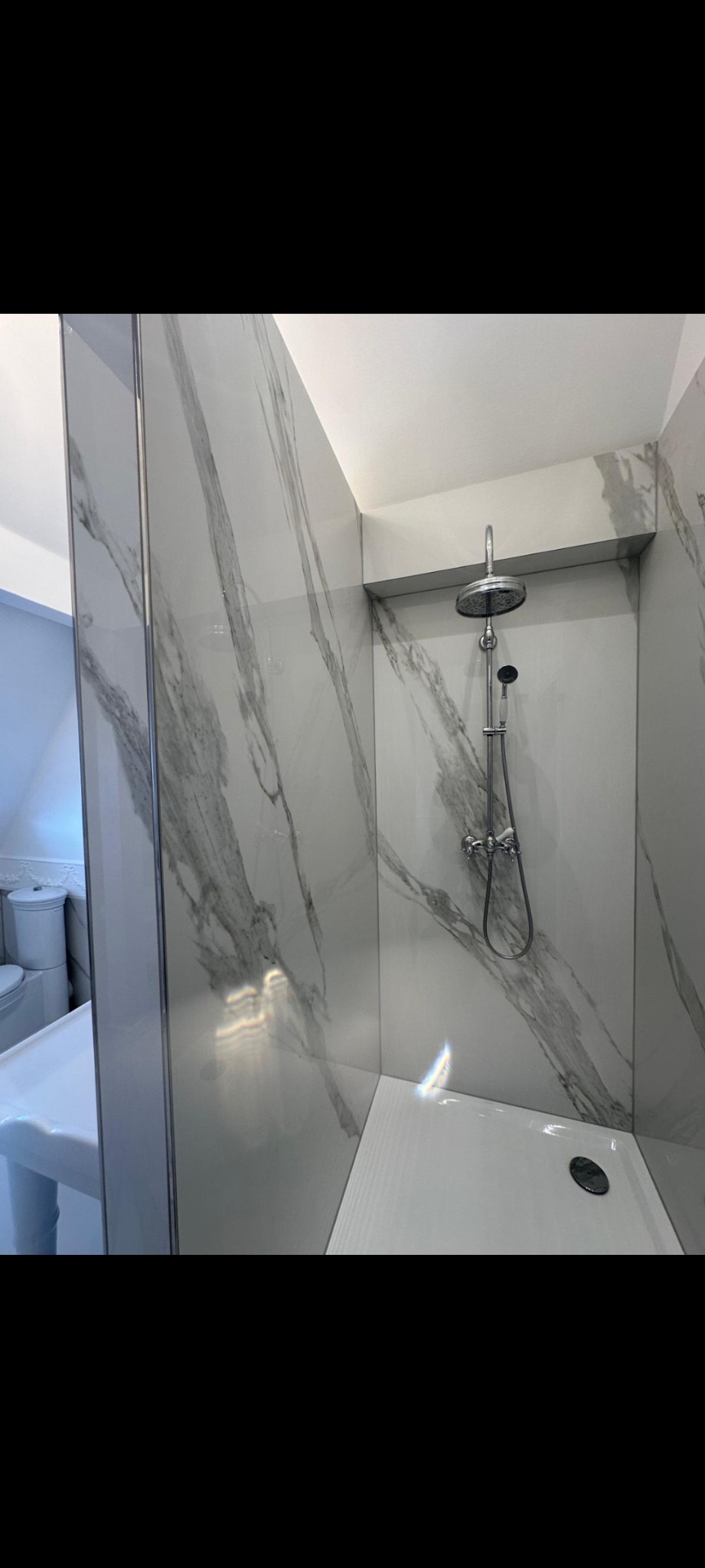 Nowoczesna kabina prysznicowa z marmurowymi płytkami, chromowaną armaturą i odpływem liniowym. Minimalistyczny design, jasne oświetlenie.