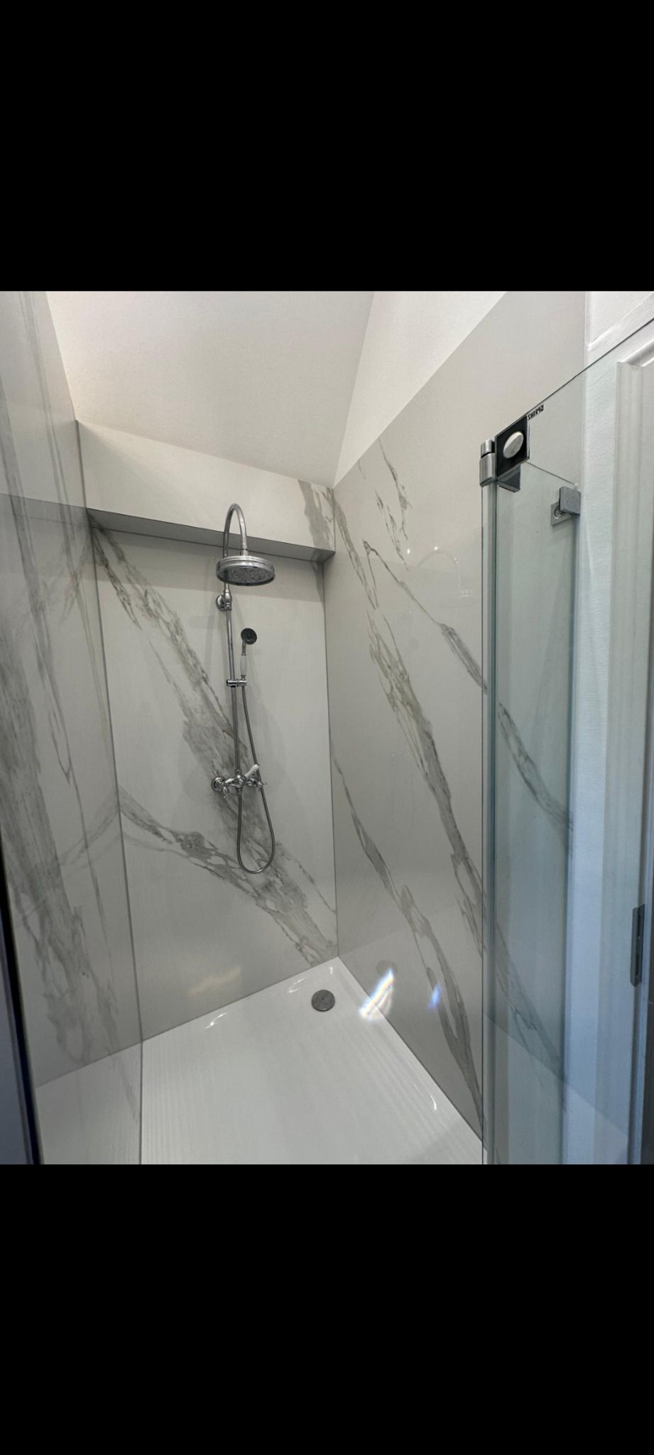 Nowoczesna kabina prysznicowa z marmurowymi płytkami, deszczownicą i szklanymi drzwiami. Minimalistyczny design, jasne kolory, widoczny odpływ liniowy.