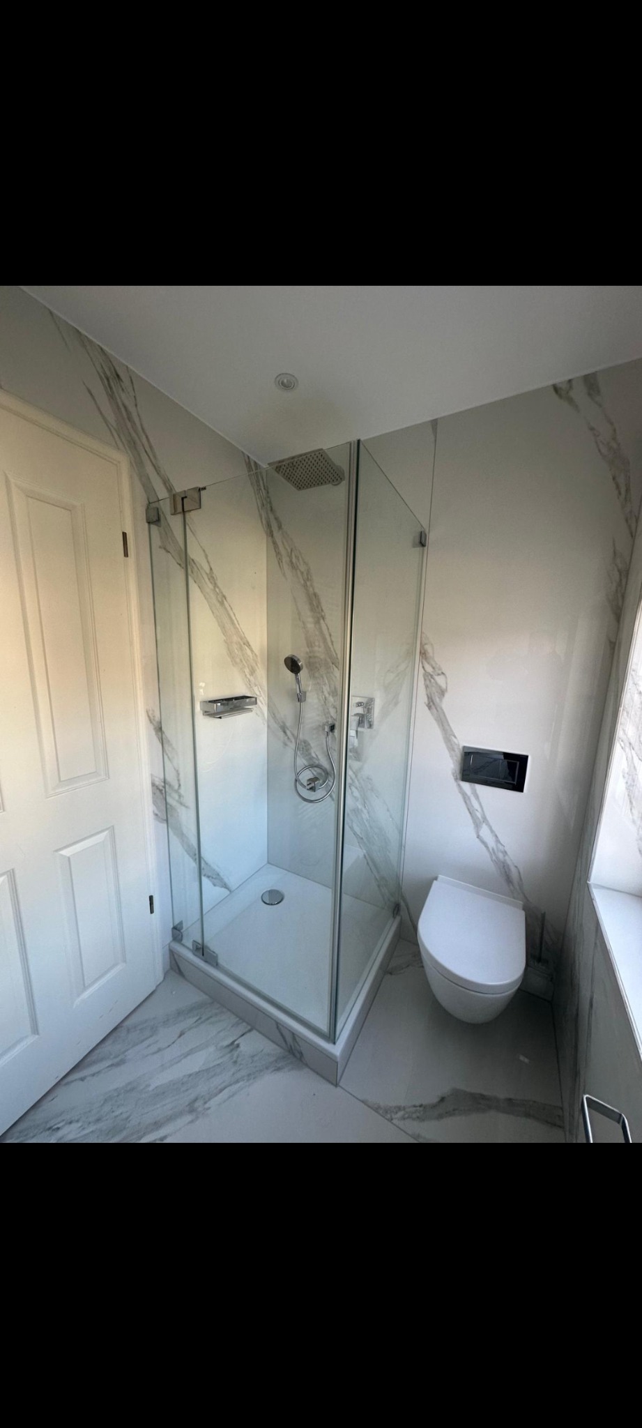 Wykończona łazienka z kabiną prysznicową typu walk-in, podwieszaną toaletą i marmurowymi płytkami na ścianach i podłodze. Nowoczesny design.