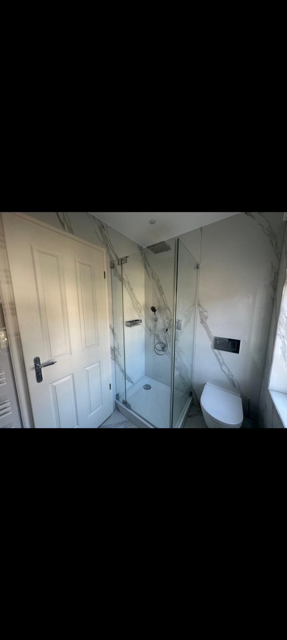 Nowoczesna łazienka z kabiną prysznicową typu walk-in, toaletą i drzwiami. Ściany wykończone płytami imitującymi marmur. Minimalistyczny design, jasne wnętrze.