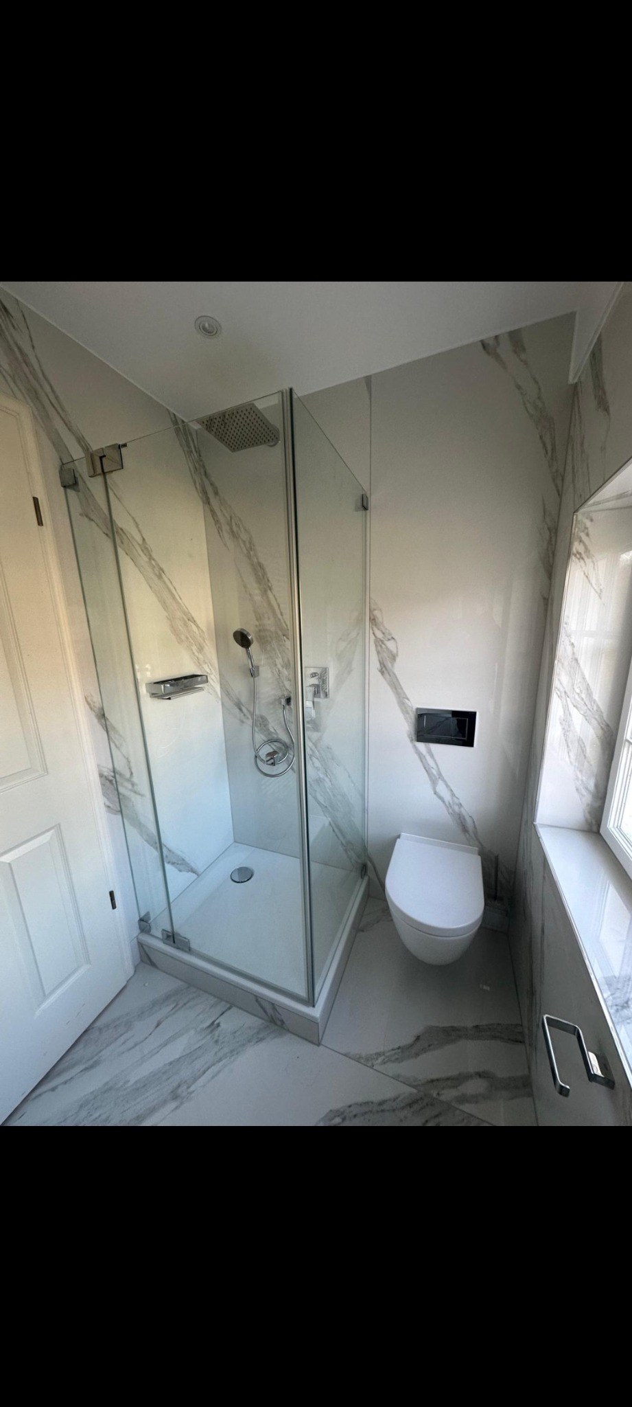 Nowoczesna łazienka z kabiną prysznicową typu walk-in, toaletą podwieszaną i marmurowymi płytkami na ścianach i podłodze. Minimalistyczny design, chromowane detale.