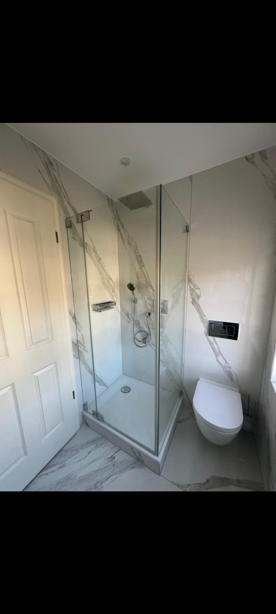 Nowoczesna łazienka z kabiną prysznicową typu walk-in, białą toaletą podwieszaną i marmurowymi płytkami na ścianach i podłodze. Minimalistyczny design.