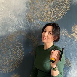EMDekor - Dekoracyjna ściana z efektem ombre i złotymi ornamentami. Kobieta trzyma szpachelkę, prezentując efektowną technikę wykończenia wnętrz.