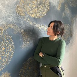 EMDekor - Dekoracyjna ściana z efektem ombre w odcieniach szarości i złota, zdobiona ornamentami. Kobieta opiera się o ścianę, prezentując efekt finalny.