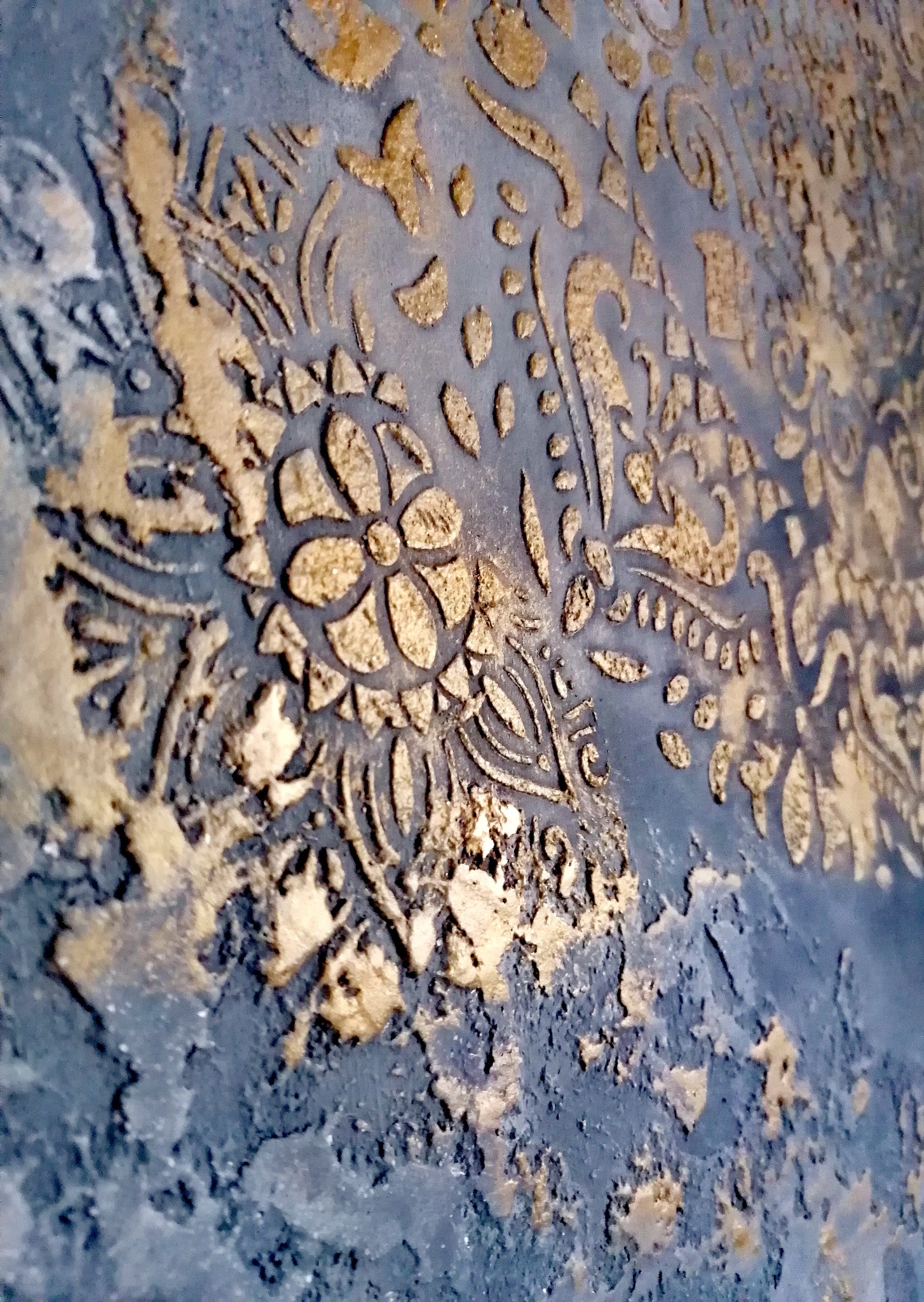 Dekoracyjna ściana z efektem strukturalnym w odcieniach szarości i złota, z wyraźnym wzorem kwiatowym i ornamentami. Wykończenie z bliska, ukazujące detale faktury.