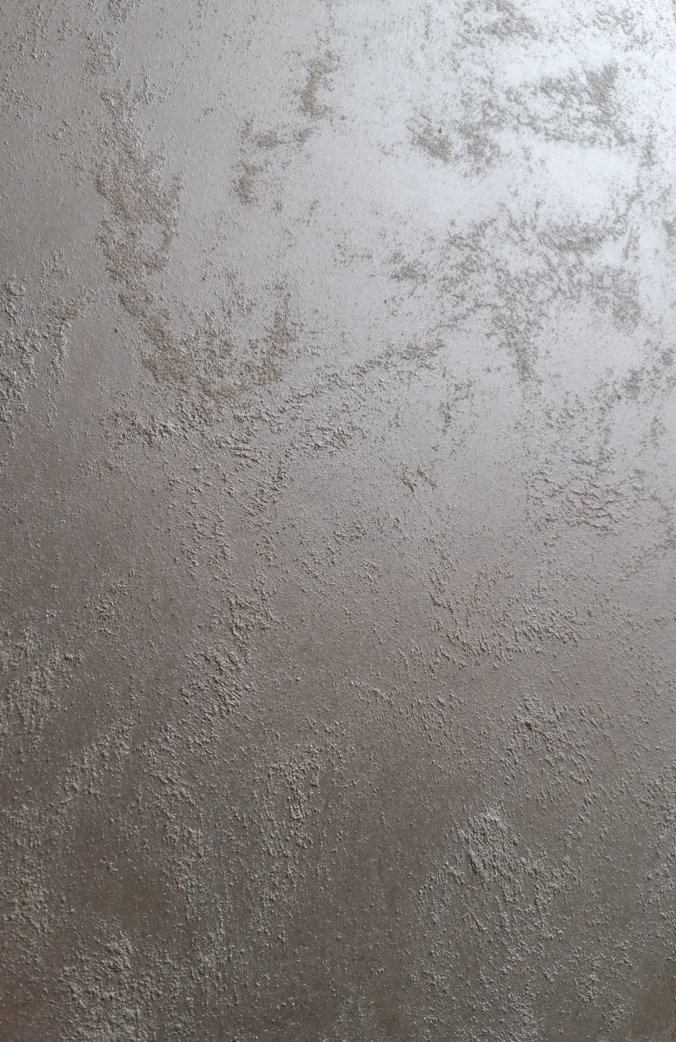Szara ściana z dekoracyjną fakturą, imitującą efekt chmur lub marmuru, z widocznymi nierównościami i subtelnym połyskiem.