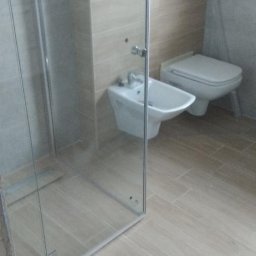 Usługi ogólnobudowlane - Nowoczesna łazienka z kabiną prysznicową typu walk-in, bidetem i toaletą. Beżowe płytki podłogowe i ścienne tworzą spójną, minimalistyczną przestrzeń.