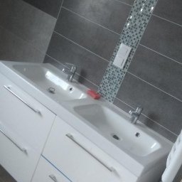 Usługi ogólnobudowlane - Nowoczesna łazienka: biała szafka z dwiema umywalkami, szara ściana z poziomymi płytkami i dekoracyjnym pasem mozaiki. Minimalistyczny design.