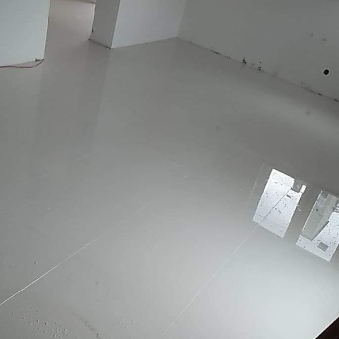 Błyszcząca, jasnoszara podłoga z płytek w pustym pomieszczeniu z białymi ścianami. Widoczne refleksy światła na gładkiej powierzchni. Minimalistyczny design.