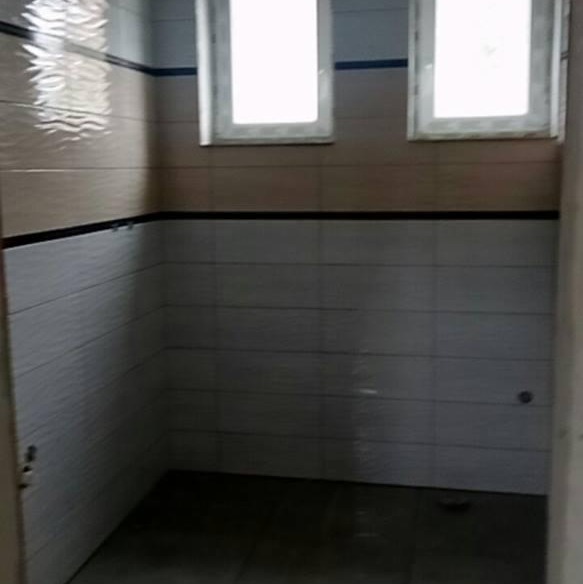 Wykończona łazienka z dwoma oknami, wyłożona kafelkami w odcieniach beżu i szarości z czarnym pasem, widok z wejścia.