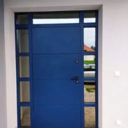 Nowoczesne, niebieskie drzwi wejściowe z bocznymi przeszkleniami, widoczne z zewnątrz, z kostką brukową u dołu i białym tynkiem na ścianie budynku.