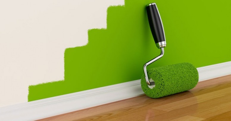 Świeżo pomalowana, zielona ściana z wałkiem do malowania, widoczne ślady białej farby na górze, drewniana podłoga przy listwie przypodłogowej.