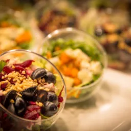 Szklane miseczki z warstwową sałatką: buraki, zielenina, ciemne winogrona i posiekane orzechy, ustawione na białym blacie, oświetlone ciepłym światłem.