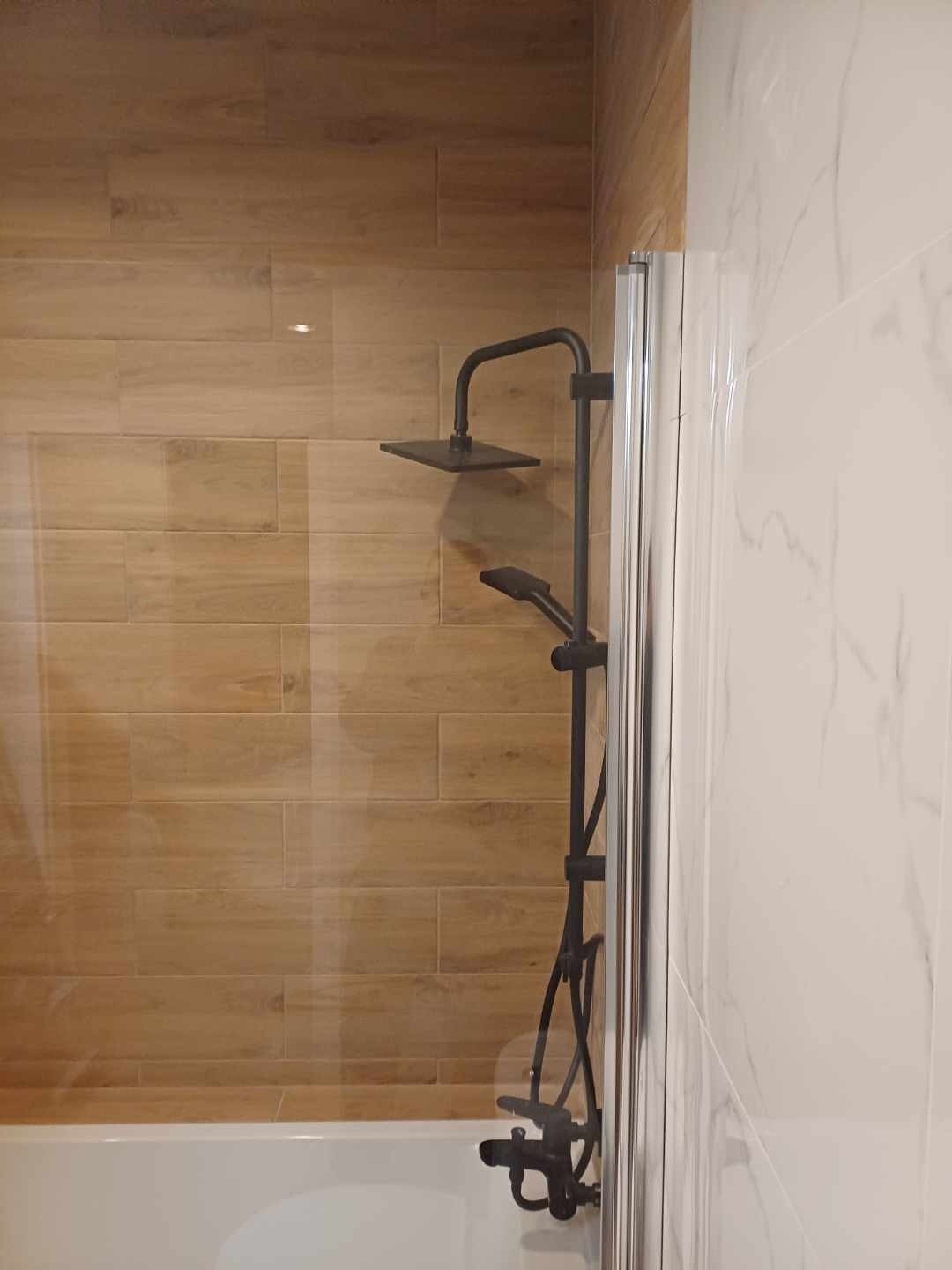 Nowoczesna kabina prysznicowa z czarną armaturą na tle drewnopodobnych płytek i białego marmuru.