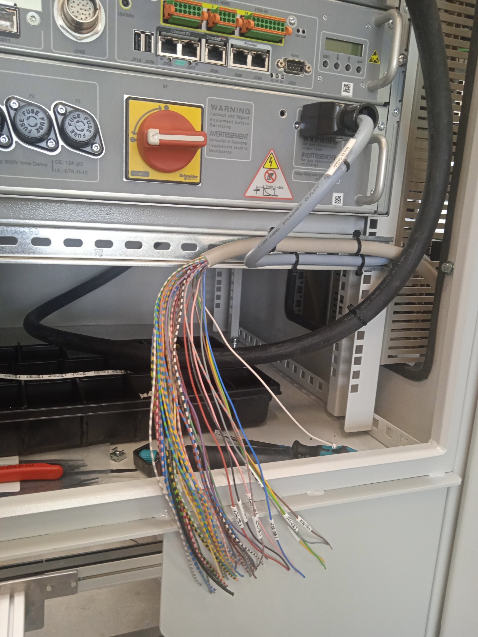 Panel sterowania z rozłączonymi, oznaczonymi przewodami, widoczne narzędzia i ostrzeżenia na panelu.