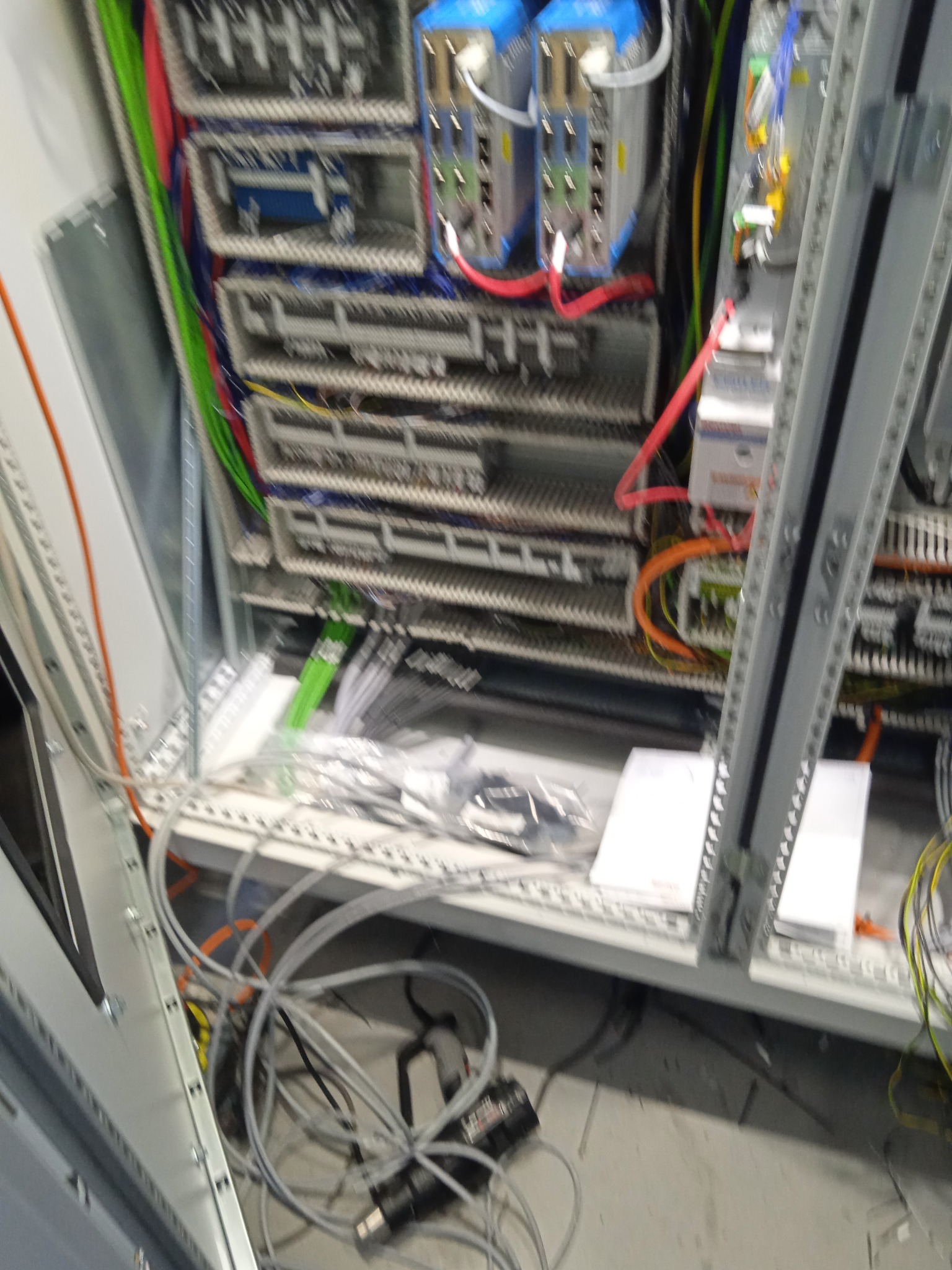 Otwarta szafa sterownicza z widocznymi modułami, przewodami w różnych kolorach oraz elementami montażowymi, częściowo rozłożona na podłodze, sugerująca etap prac instalacyjnych.