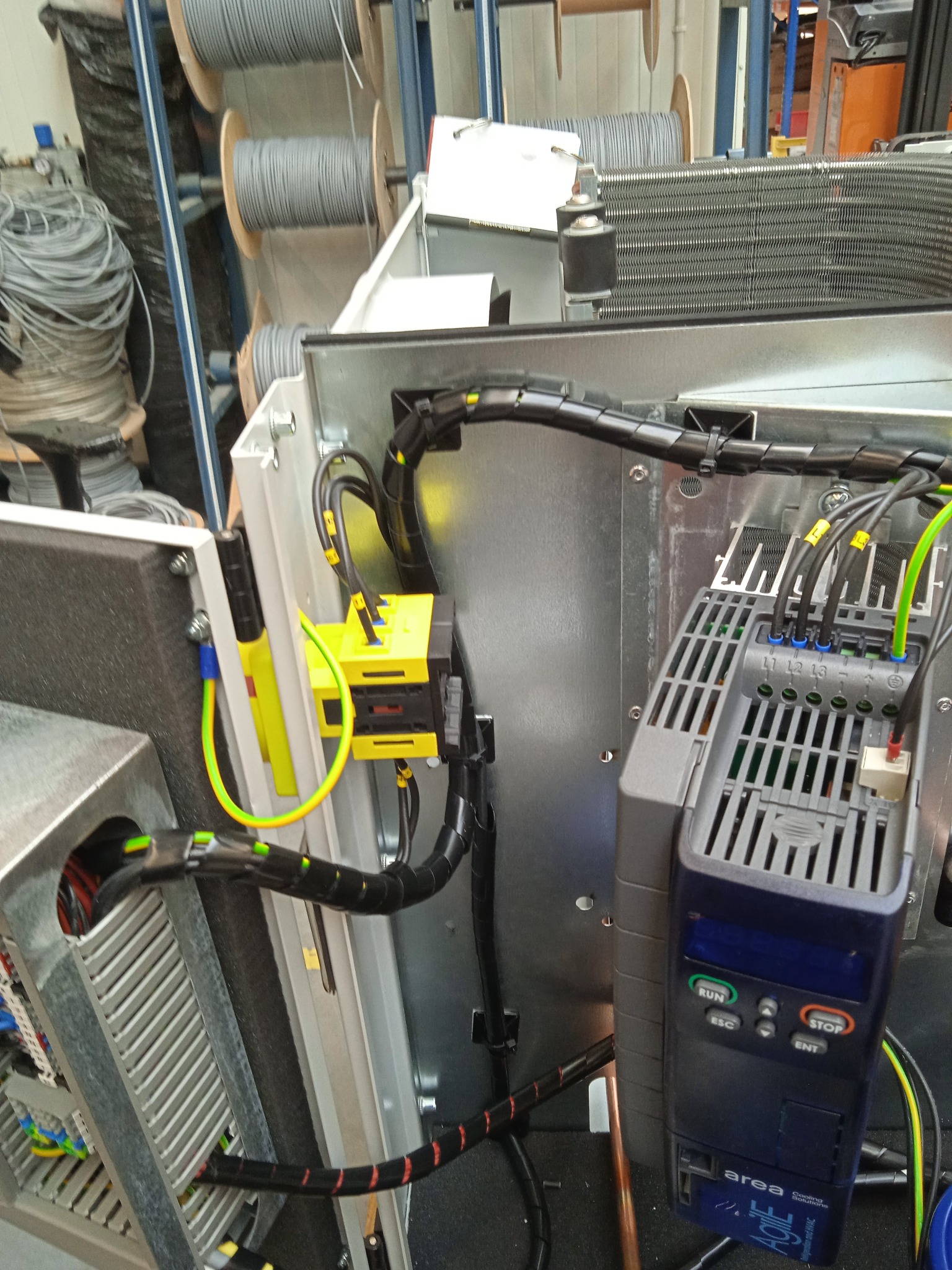 Szczegółowe ujęcie wnętrza szafy sterowniczej z widocznymi elementami: falownik Area Agile Cooling Solutions, czarne peszle ochronne, przewody oznaczone etykietami, oraz złącza elektryczne...