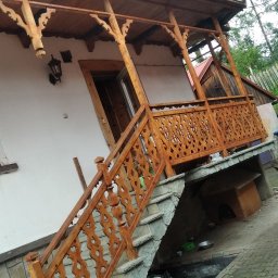 Złota raczka - Drewniany, zdobiony ganek z balustradą w stylu regionalnym, prowadzący do wejścia domu w Rokicinach Podhalańskich. Schody wyłożone kamieniem, widoczny fragment podwórka.