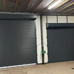 Dwie zamknięte, szare bramy rolowane wewnątrz garażu, z widocznymi elementami konstrukcyjnymi sufitu i ścian.