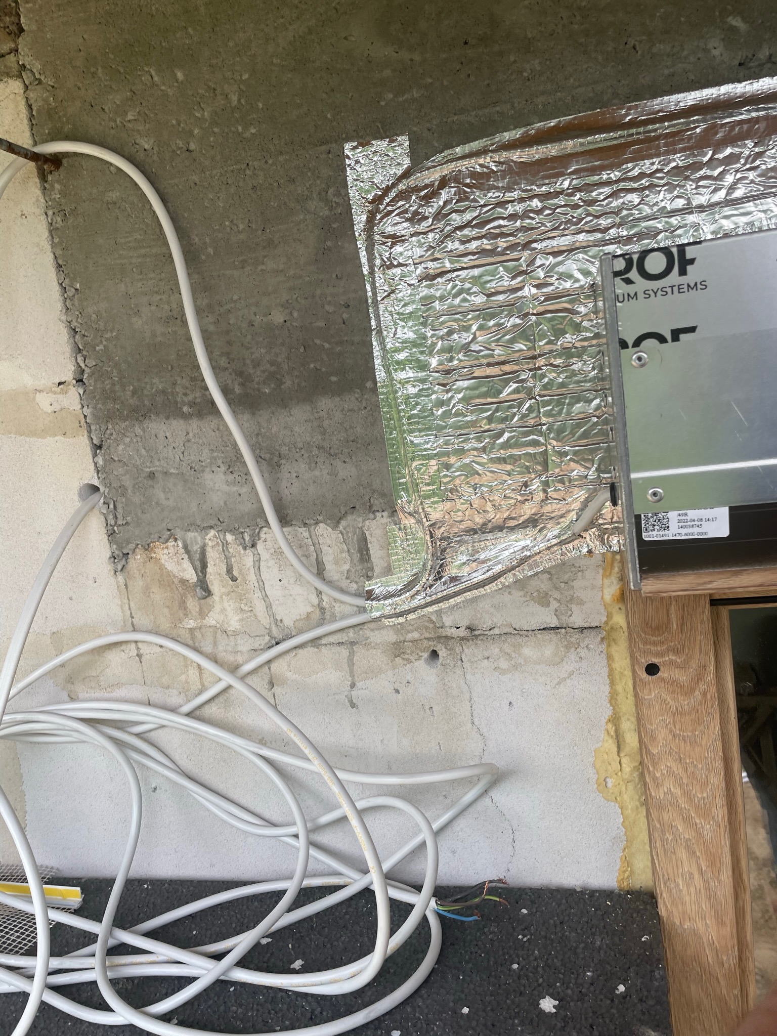 Montaż instalacji elektrycznej przy oknie, widoczne kable, izolacja termiczna z folii aluminiowej oraz fragment ramy okiennej.