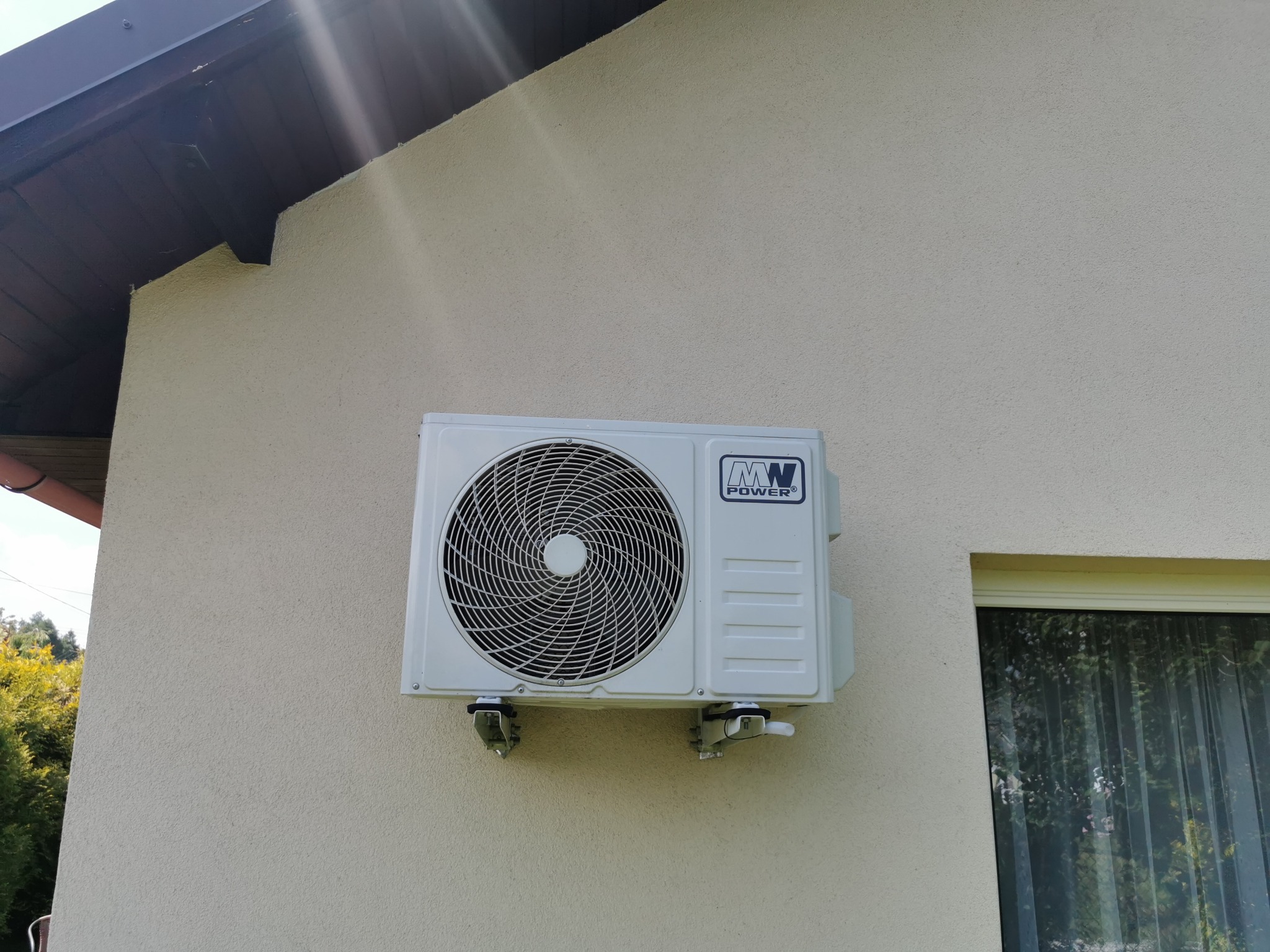 Zewnętrzna jednostka klimatyzacji marki MW Power, zamontowana na elewacji budynku w Andrychowie, widoczna z boku okna.