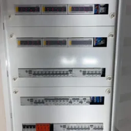 Rozdzielnica elektryczna z modułami alarmowymi Satel i zabezpieczeniami Eaton, widoczne przewody i listwy zaciskowe, zamontowana wewnątrz szafki.