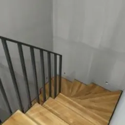 Nowoczesne schody drewniane z metalową balustradą w minimalistycznym wnętrzu, widok z góry na zakręt schodów. Szare ściany w tle.